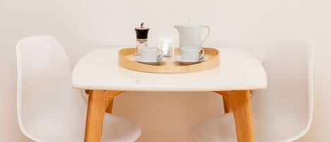 A minimalist dining setup with a white table, two white chairs, a tray with a teapot, cups, and a small container.
