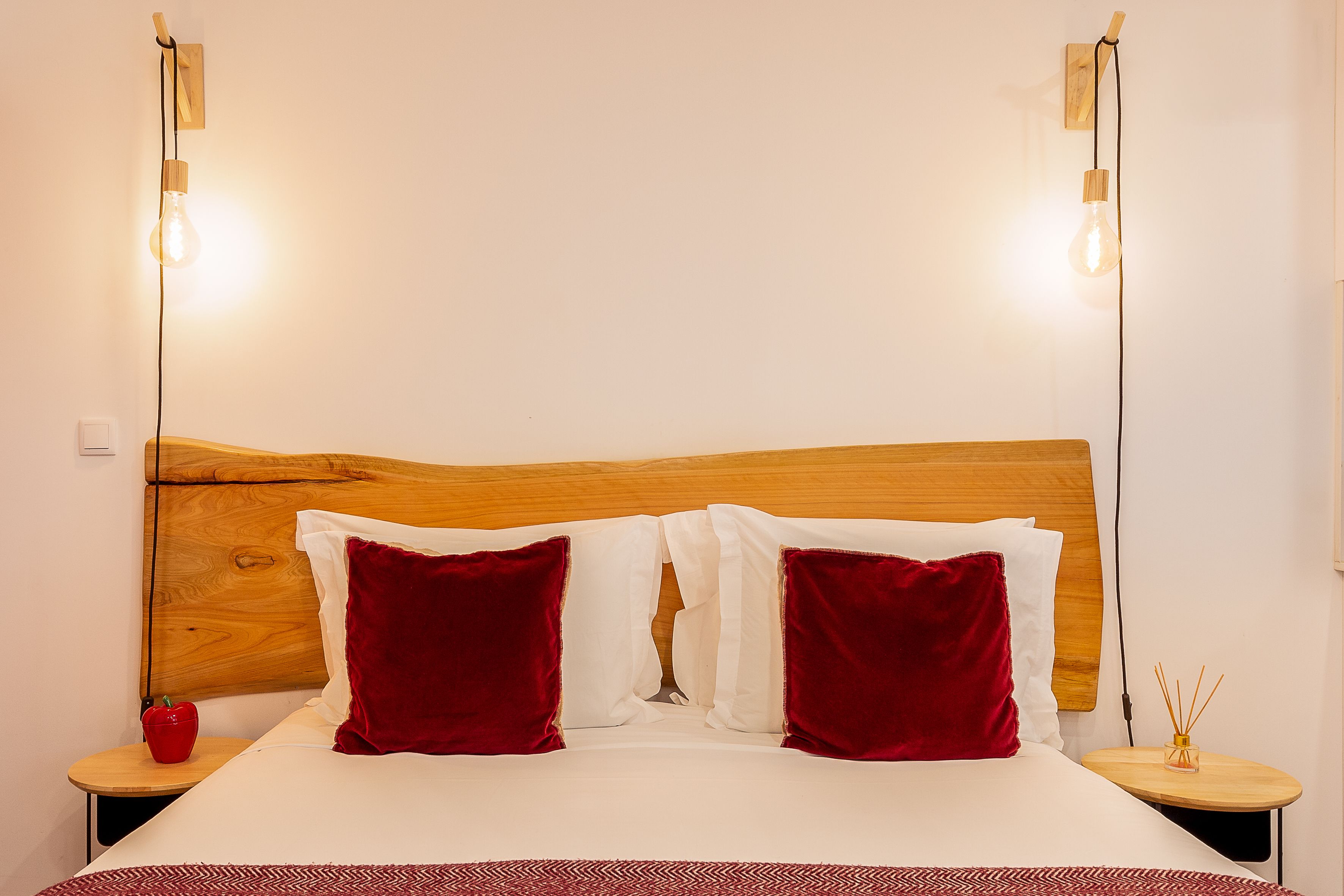 Una cama bien hecha con cabecera de madera, dos mesitas de noche con lámparas y una manzana roja sobre una de ellas.