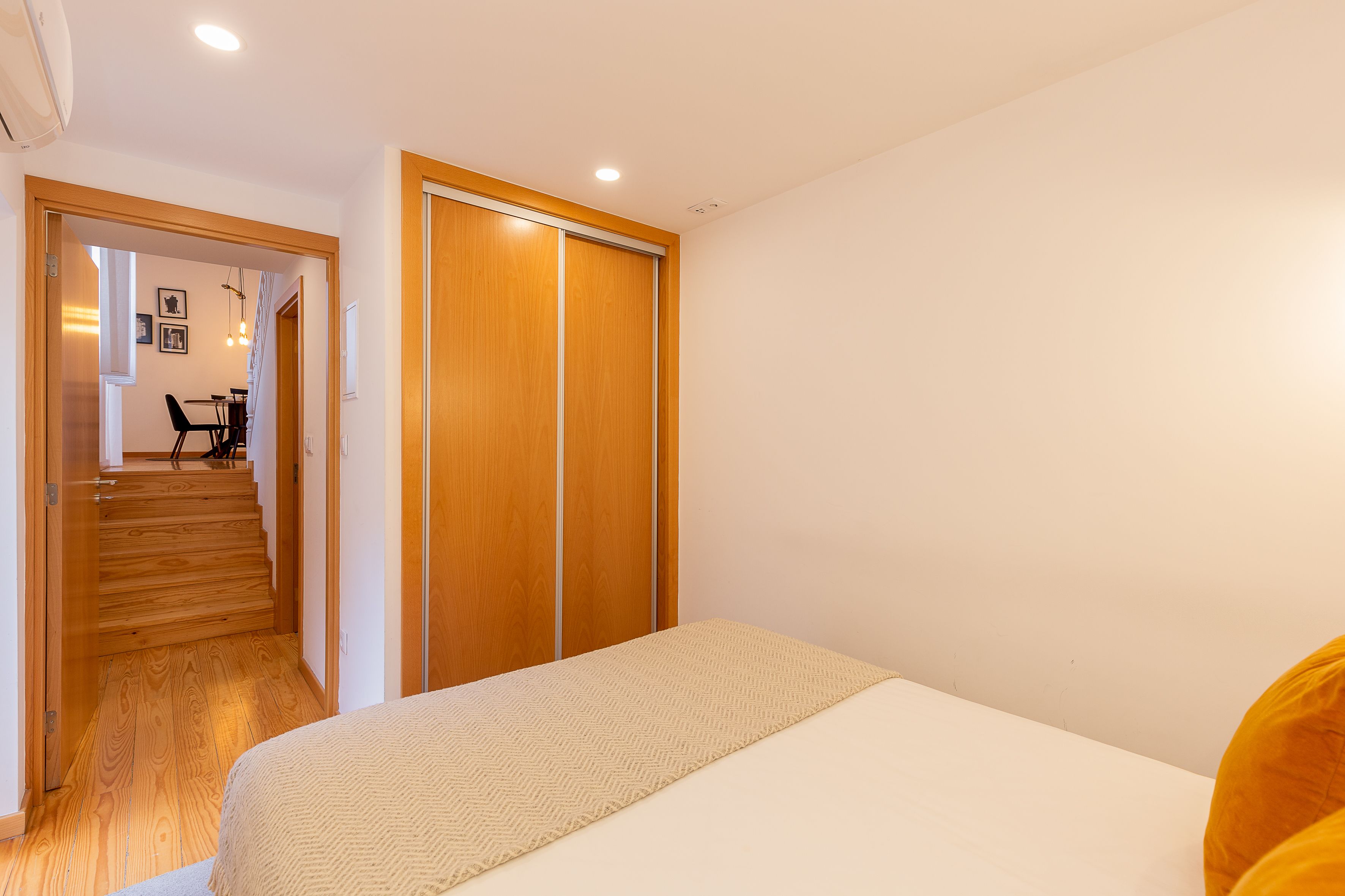 Ein Schlafzimmer mit Bett, Holzschrank und einer Treppe, die in einen Essbereich führt.