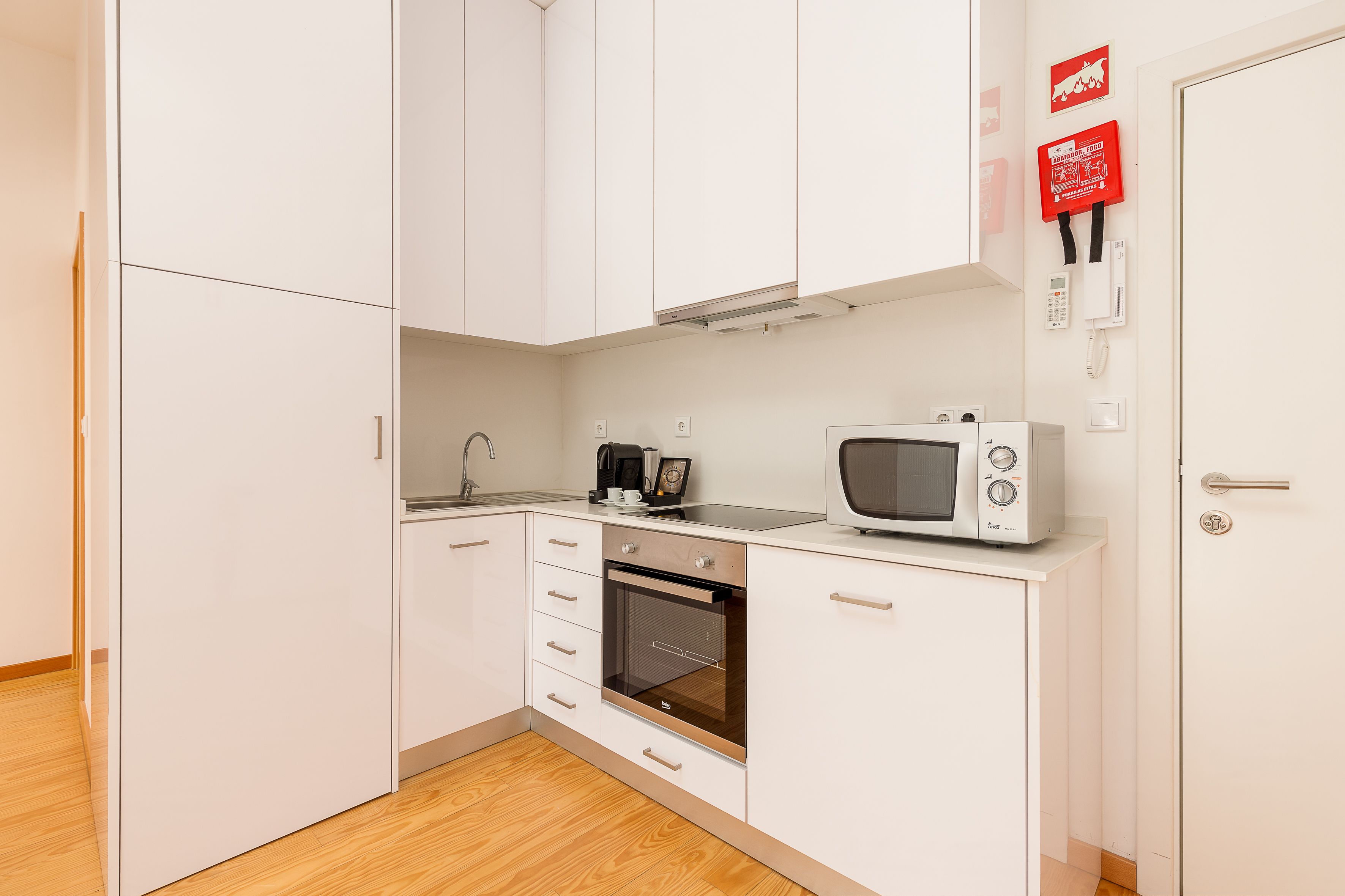 A compact kitchen with white cabinets, a built-in oven, a microwave, and a coffee maker.