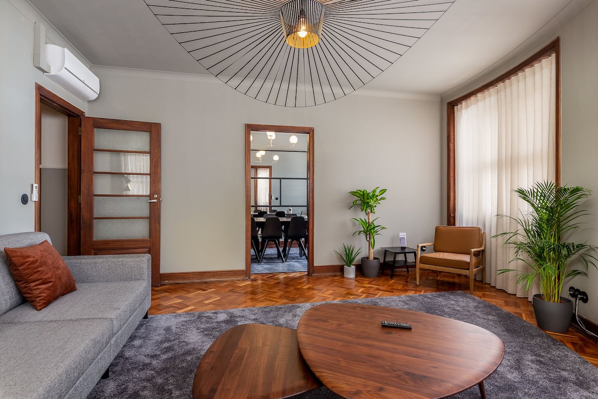 Een moderne woonkamer met een bank, salontafel en stoelen, een eethoek met tafel en stoelen, en een grote spiegel die de ruimte weerspiegelt.