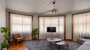 A modern living room with a flat-screen TV, a grey sofa, a brown leather chair, and a grey rug. - YOUROPO - Santa Catarina (Porto)
