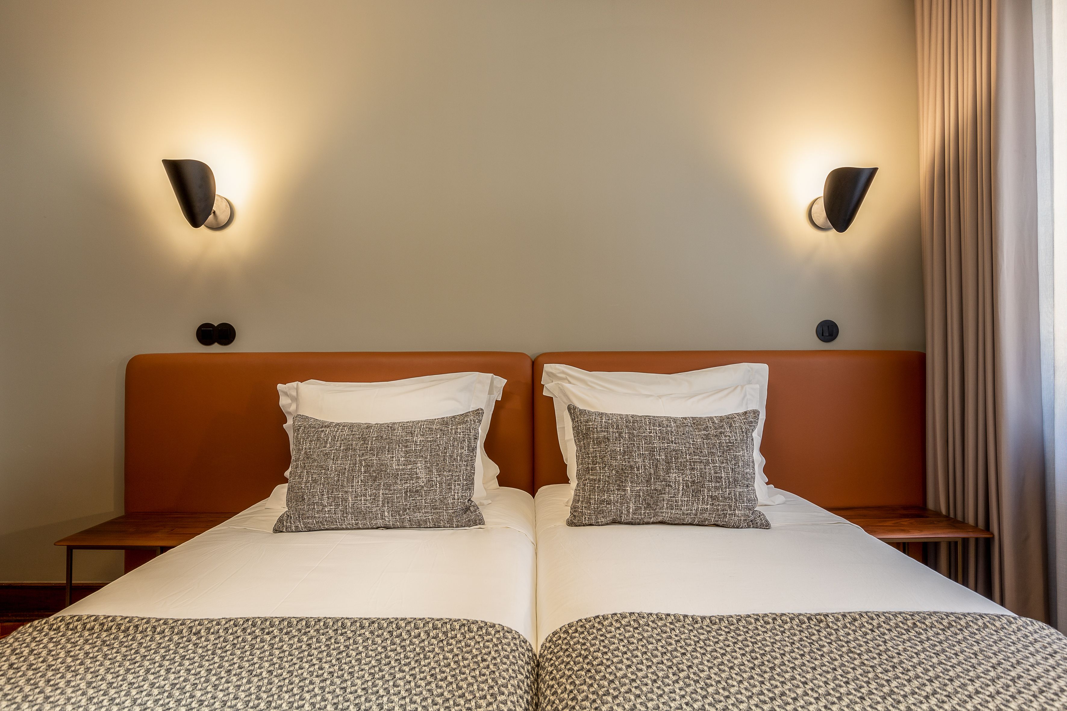 A double bed with a patterned bedspread, two pillows, and a wooden headboard. There are two wall-mounted light fixtures on either side of the bed.
