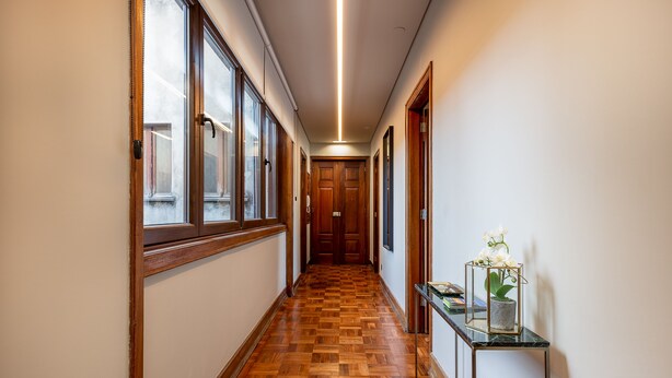 A hallway with wooden flooring, a glass display case with an orchid, and a door at the end. - YOUROPO - Santa Catarina (Porto)