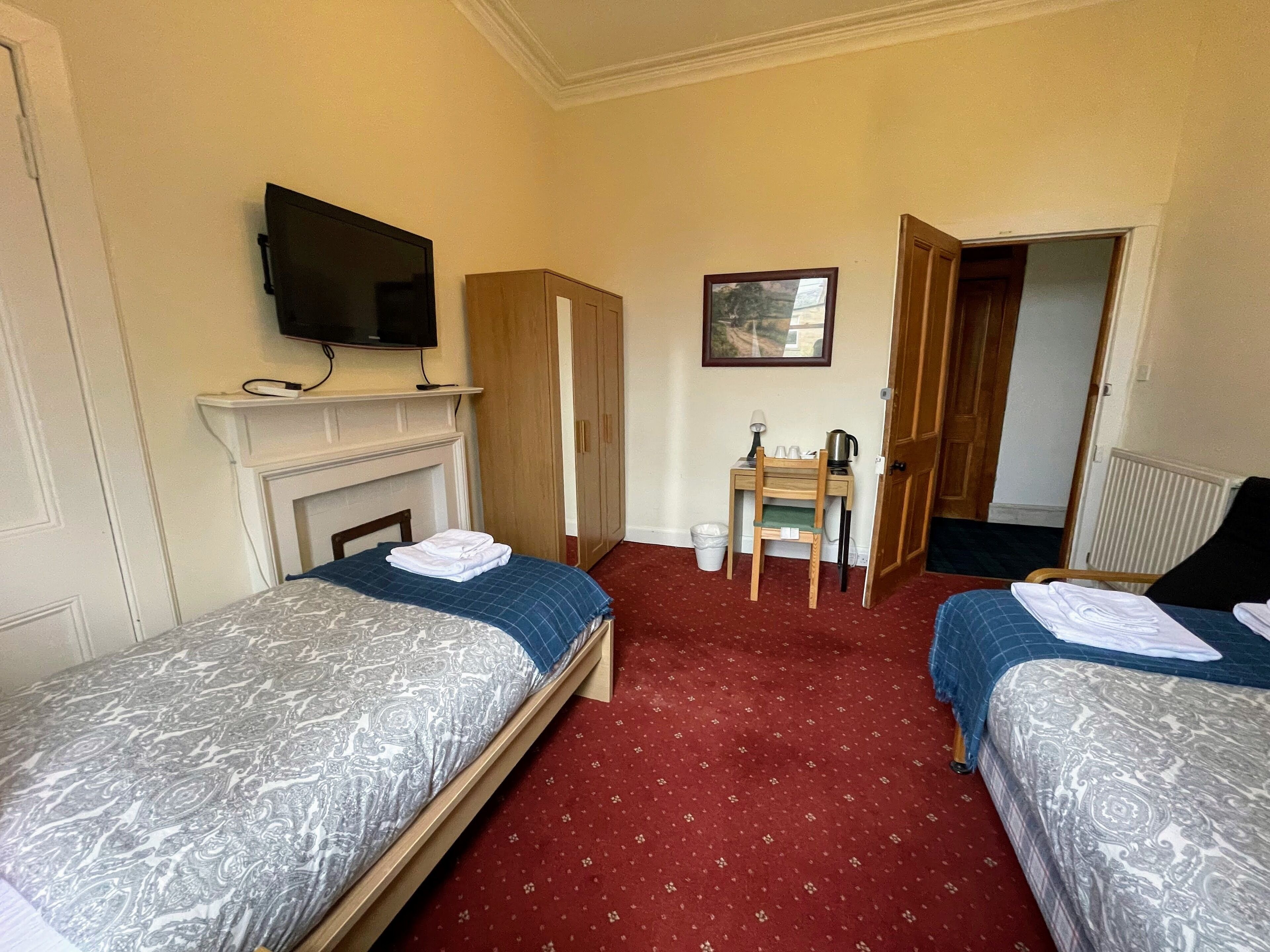 A hotel room with two beds, a television, a small table with a chair, and a fireplace.