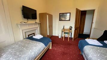 A hotel room with two beds, a television, a small table with a chair, and a fireplace.