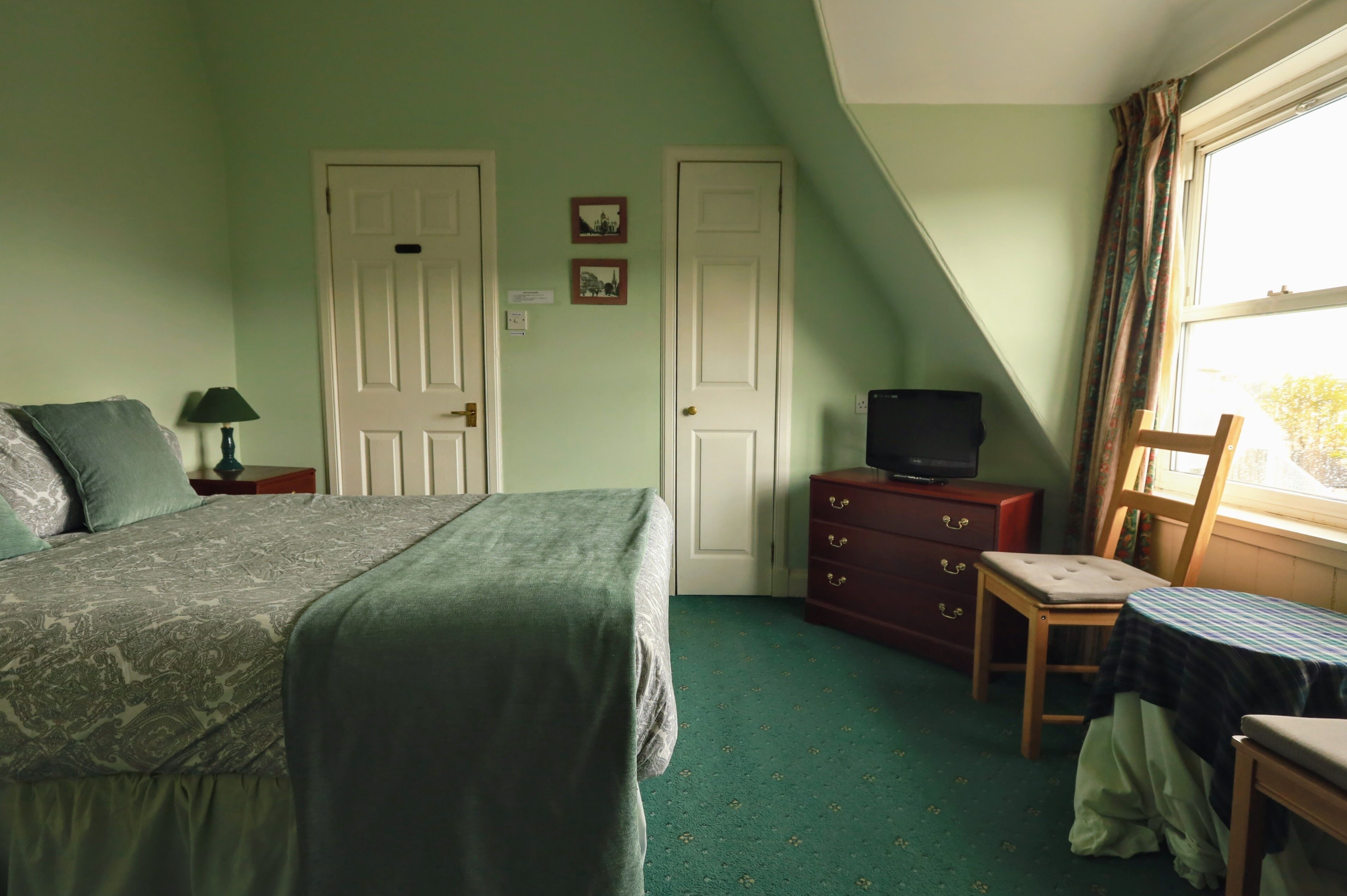 A bedroom with a bed, a dresser, a television, a chair, and a window.