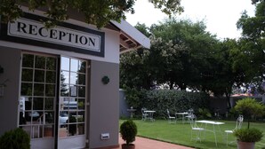 A reception area with a sign, a glass door, and a small garden with tables and chairs.