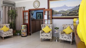 A hotel lobby with patterned armchairs, a large painting, a clock, and a reception desk.