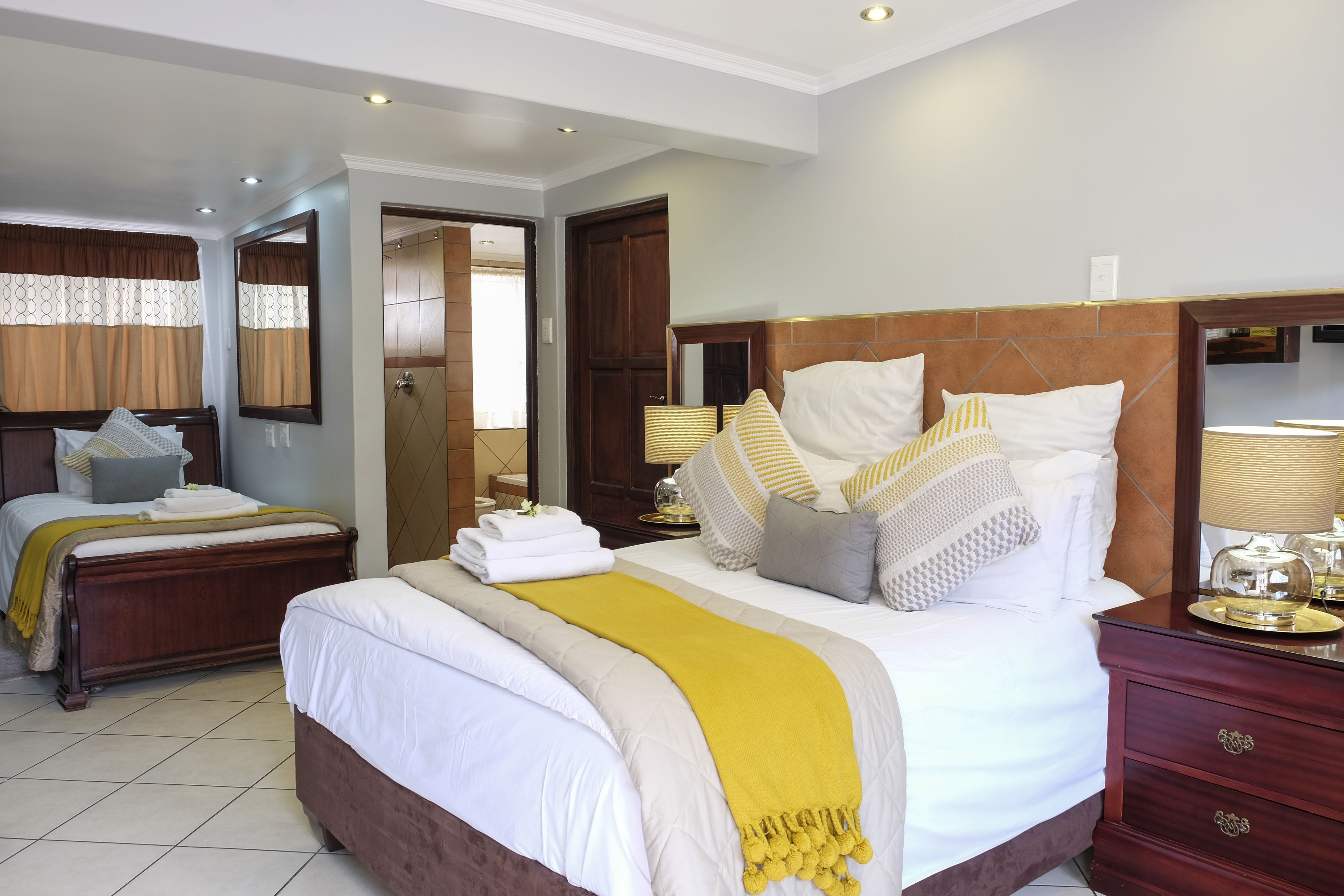A well-lit hotel room with a large bed, a wooden headboard, and a nightstand with a lamp.