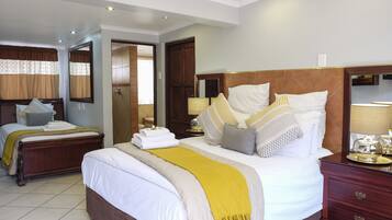 A well-lit hotel room with a large bed, a wooden headboard, and a nightstand with a lamp.