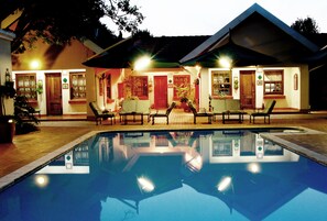 A swimming pool with lounge chairs and a building with multiple doors and windows. - Waterkloof Guest House (Pretoria)