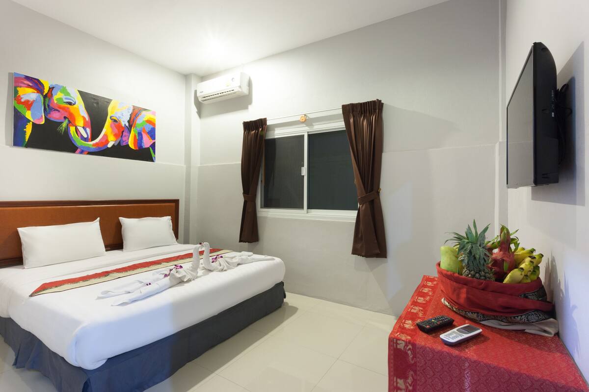 A hotel room with a bed, a TV, a fruit basket, and a painting on the wall.