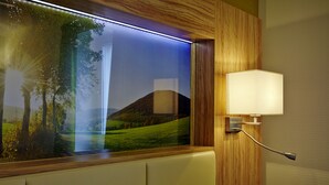 Een hotelkamer met een groot raam, een wandlamp en uitzicht op een landschap.