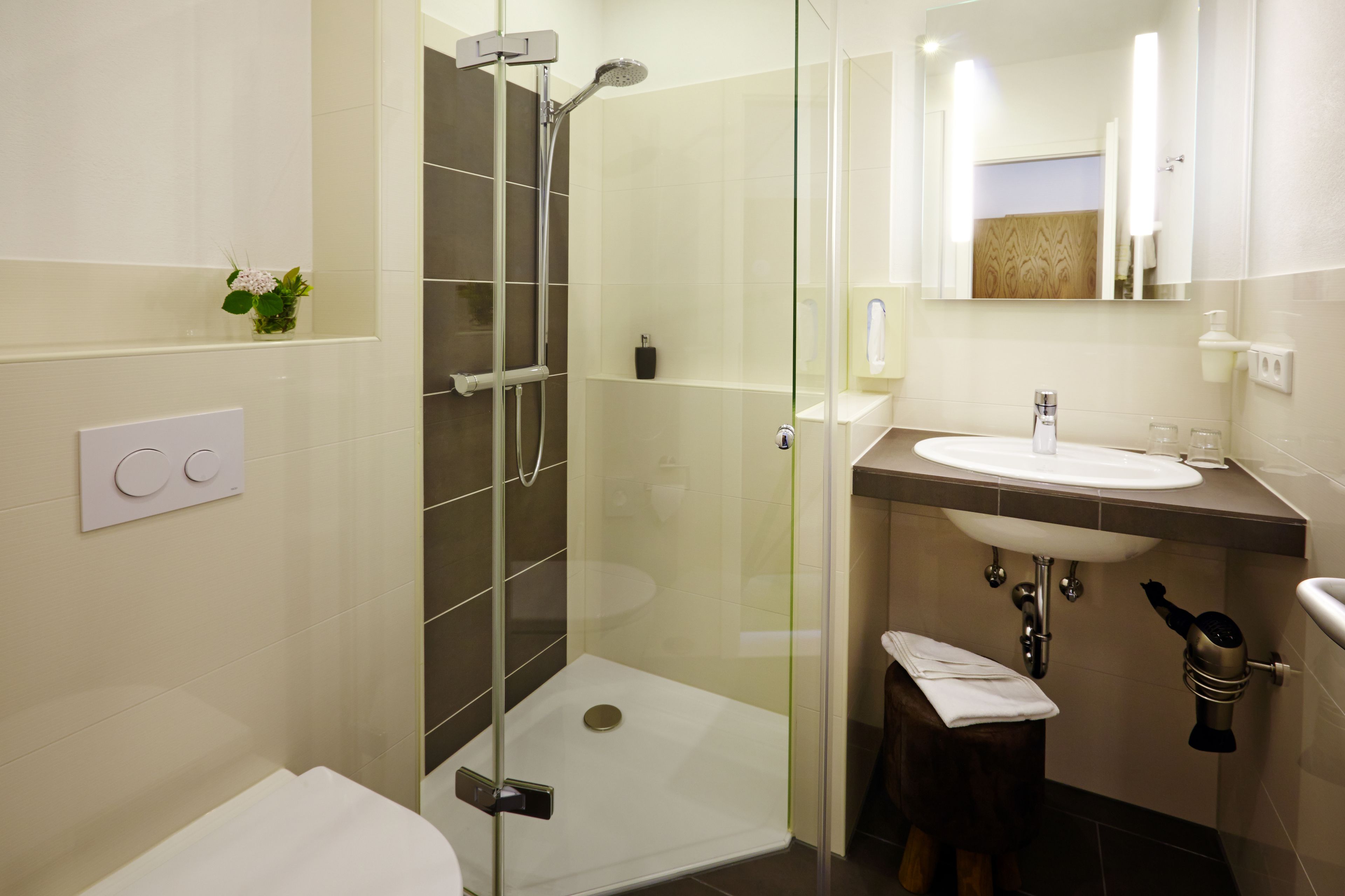 A modern bathroom with a glass-enclosed shower, a white sink, and a small stool with a towel.