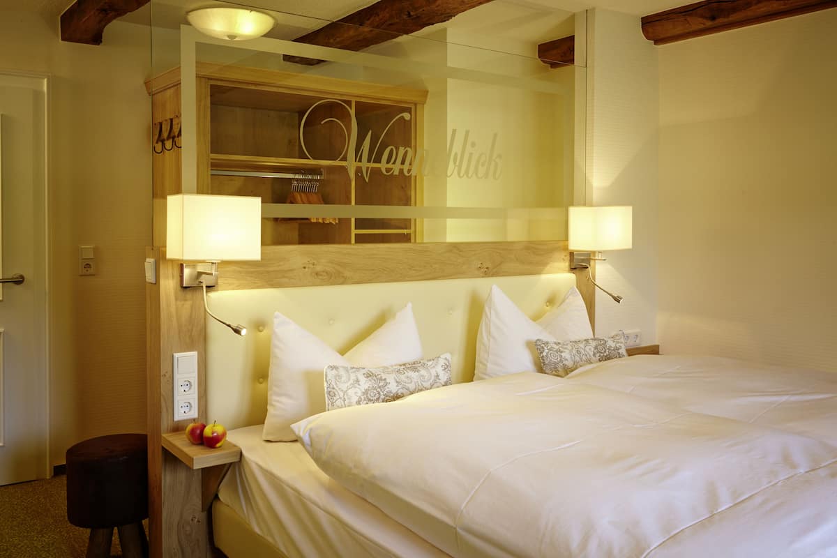 Quarto de hotel com uma cama grande, abajures, cabeceira de madeira e um espelho refletindo o quarto.
