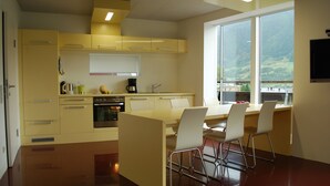 A modern kitchen with a dining area, large windows, and a view of the outdoors. - SUN Matrei Apartments (Matrei in Osttirol)