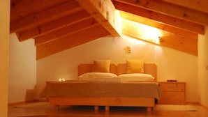 A cozy attic bedroom with a wooden bed, a nightstand, and a small table with apples. - SUN Matrei Apartments (Matrei in Osttirol)