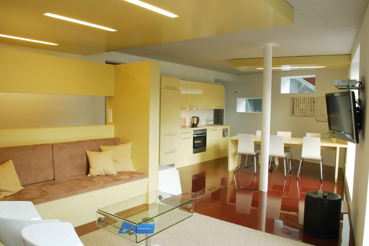 Una sala de estar moderna con una mesa de centro de vidrio, un sofá y una cocina con una mesa de comedor y sillas.