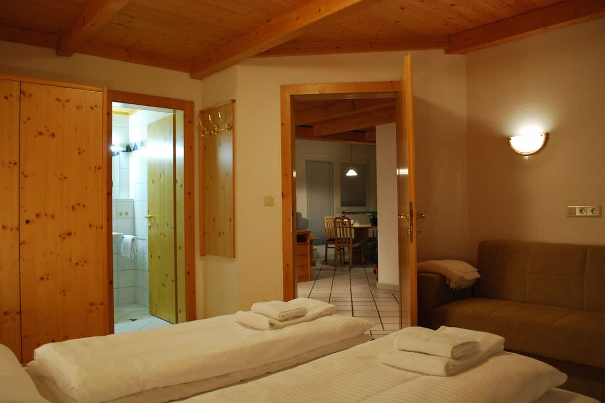 Habitación de hotel con dos camas, techo de madera, un sofá y un baño visible a través de una puerta abierta.