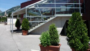 A modern building with a glass staircase leading to a second floor. There are potted plants in the foreground. - SUN Matrei Apartments (Matrei in Osttirol)