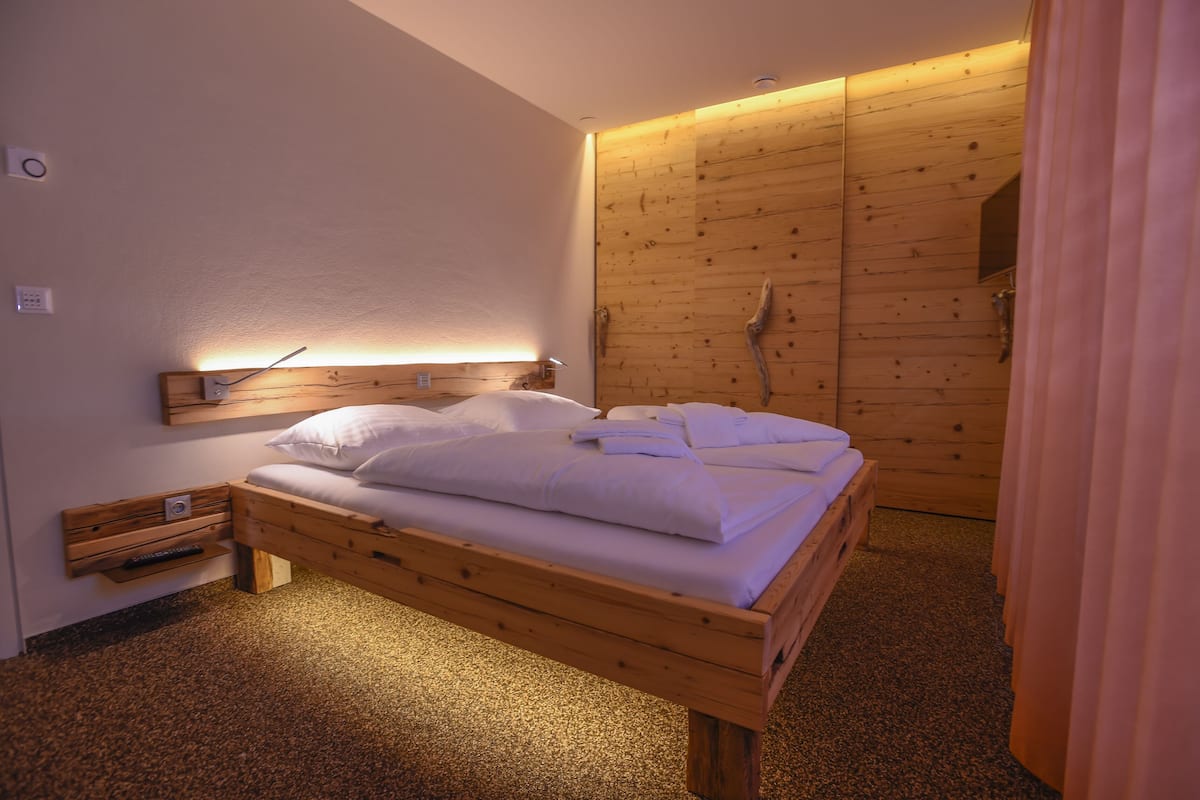 Una cama de madera con ropa de cama blanca en una habitación con pared y puerta de madera.