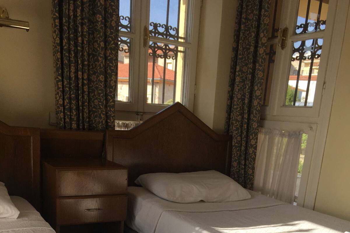 A hotel room with two beds, a wooden headboard, a nightstand, and a window with curtains.