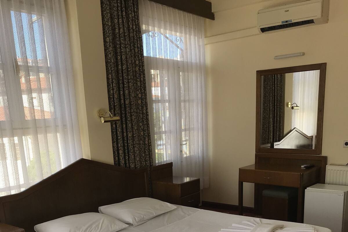 A hotel room with a neatly made bed, a bedside table, a small desk with a mirror, and a radiator.