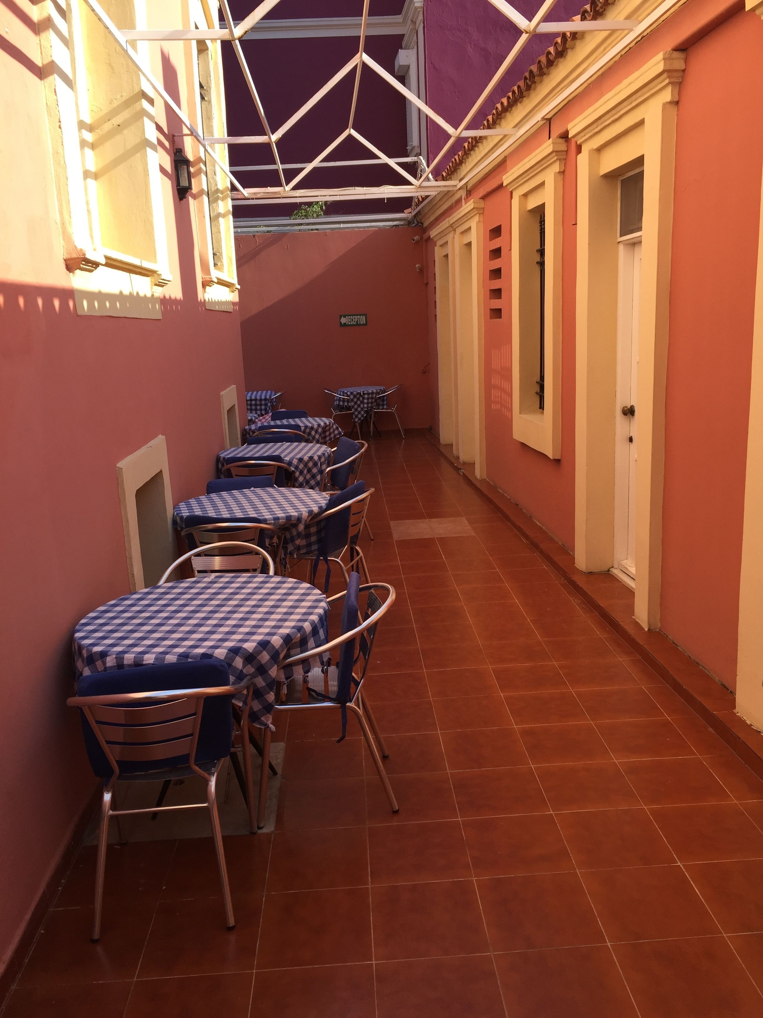 Un pasillo con mesas y sillas, un letrero que indica una zona de recepción y una puerta a la derecha.