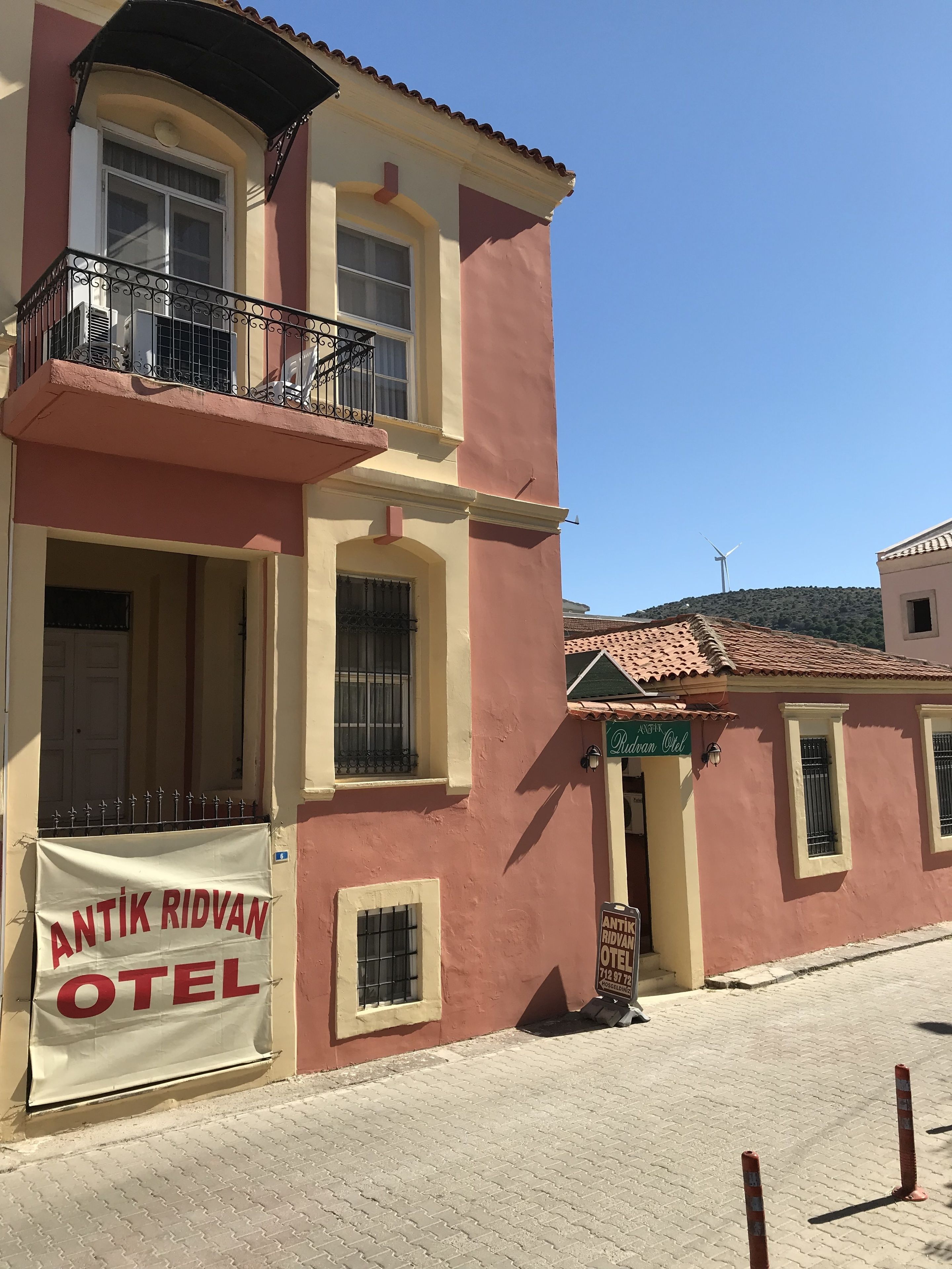 A two-story building with a sign for "Antik Ridvan Hotel" and a wind turbine in the background.