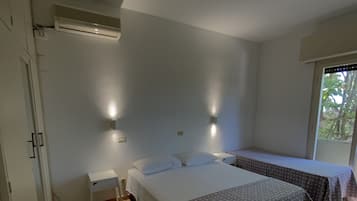 Un dormitorio con dos camas, una mesita de noche pequeña, aire acondicionado instalado en la pared y una ventana con vista a árboles.