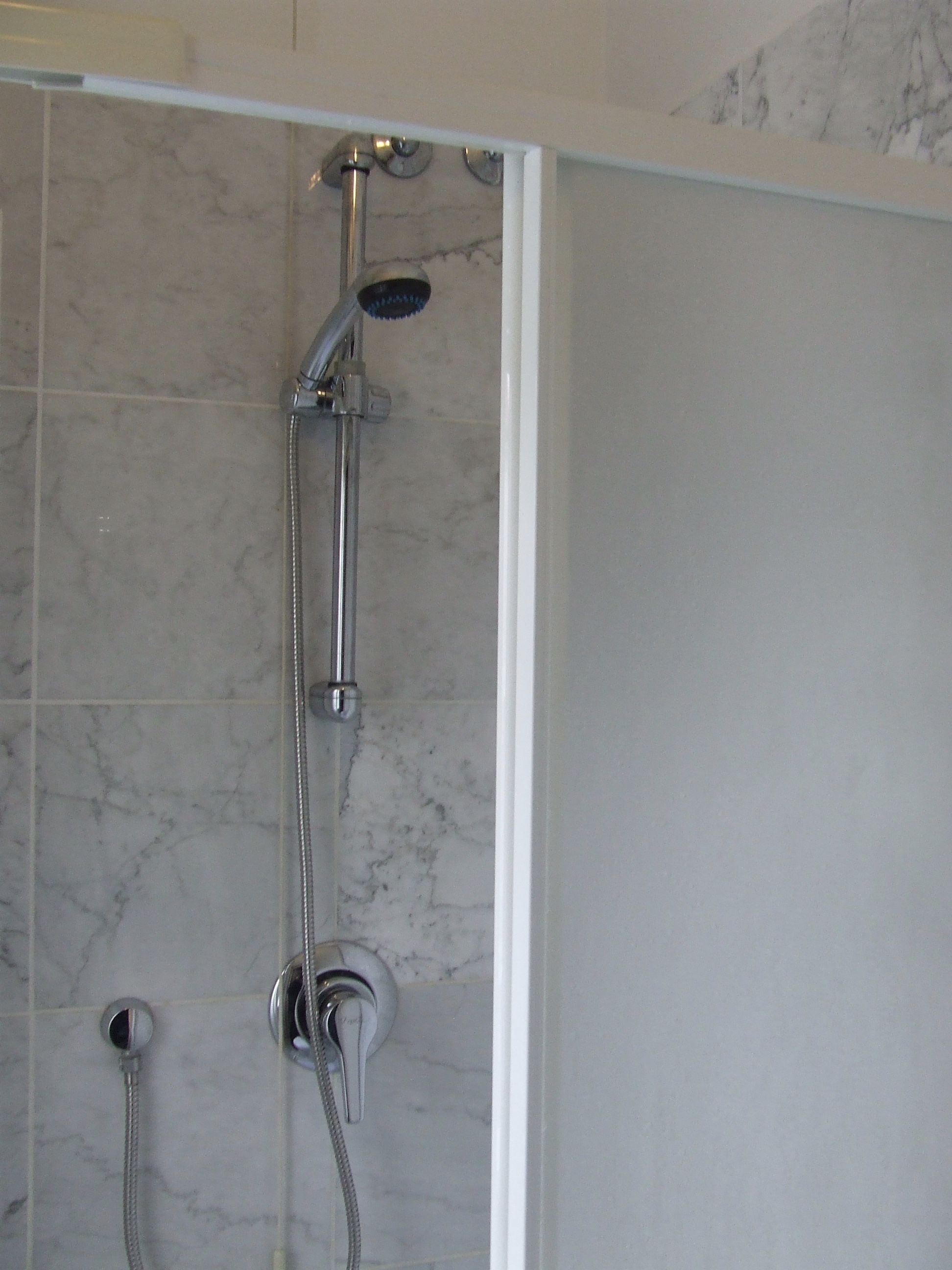 A shower with a handheld showerhead and a wall-mounted faucet.