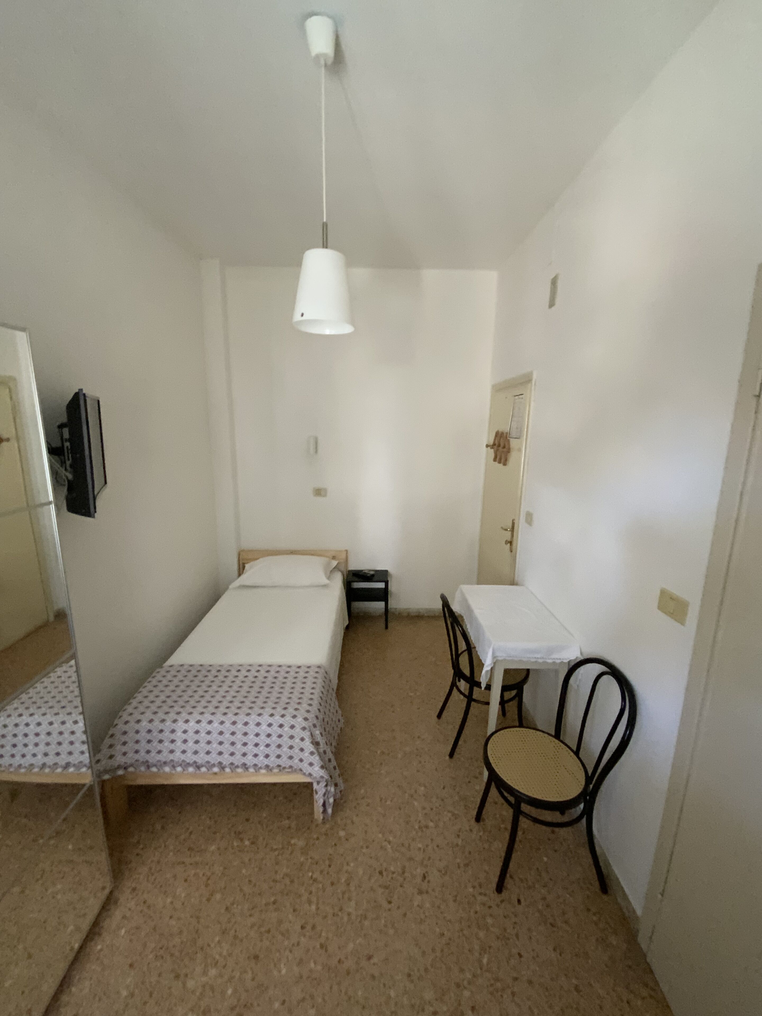 A small, sparsely furnished room with a bed, a table, and a chair.