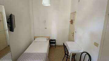 A small, sparsely furnished room with a bed, a table, and a chair.