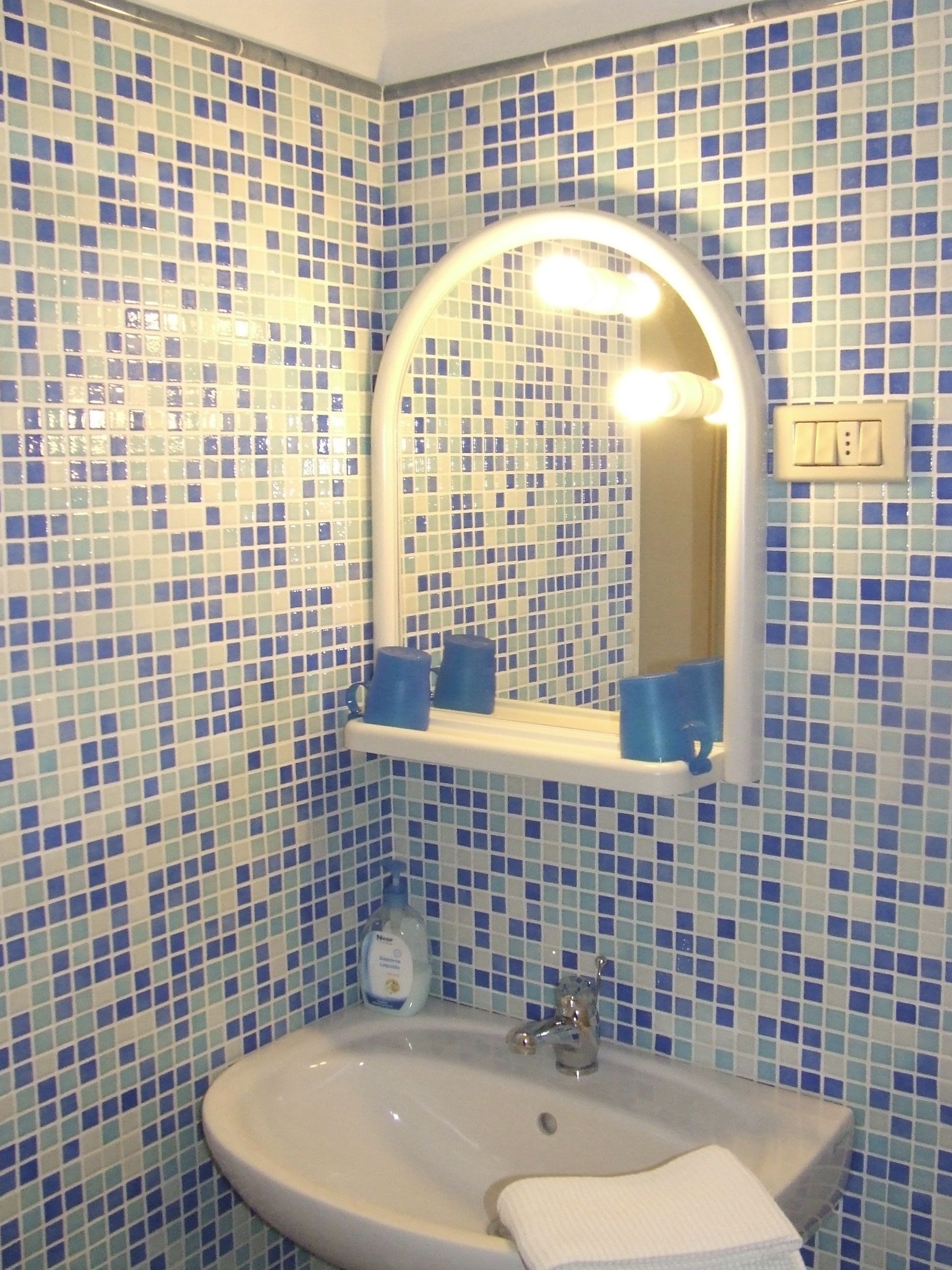 Ein Badezimmer mit Waschbecken, Spiegel und blauen Mosaikfliesen.