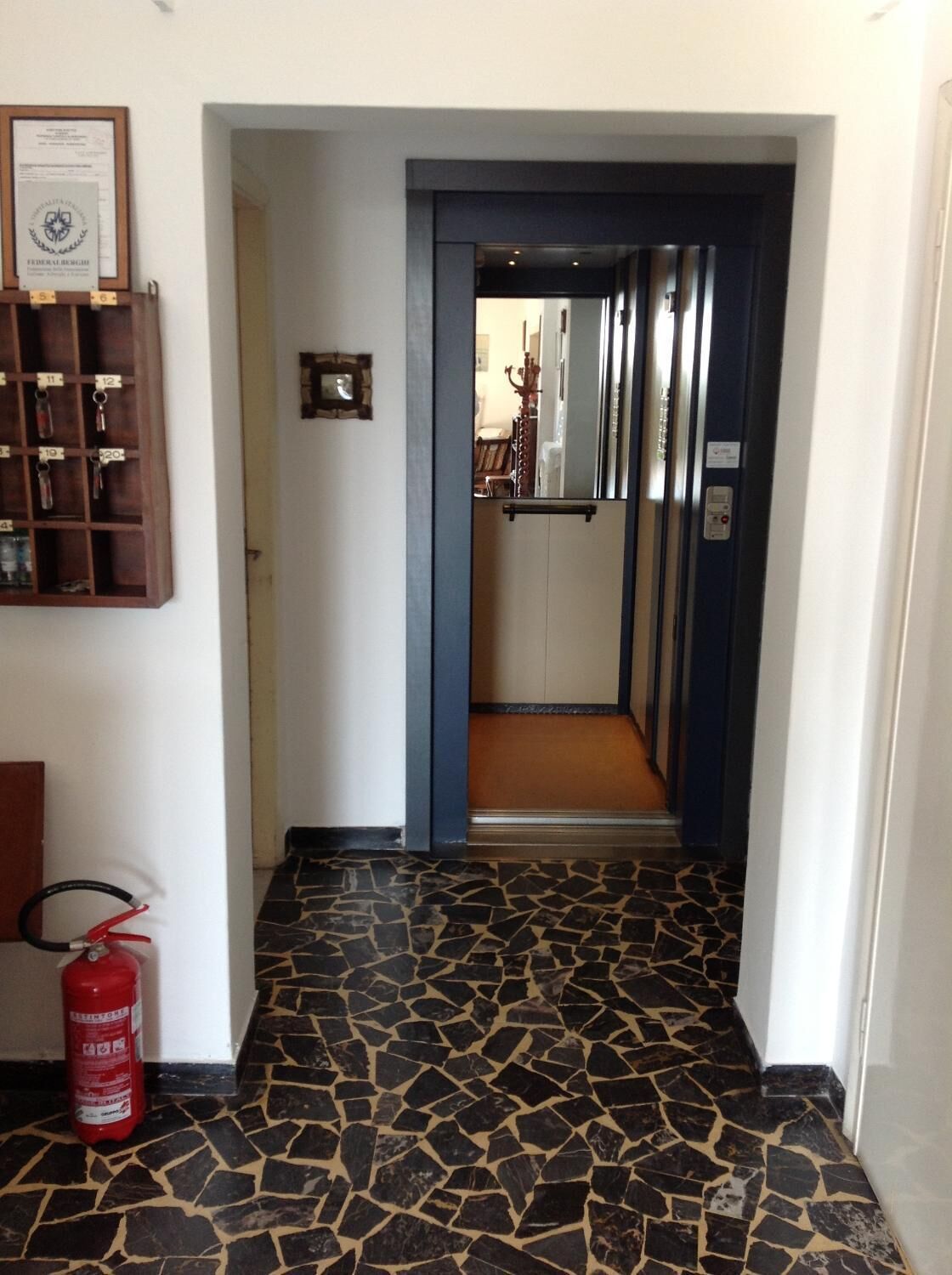 A hallway with a tiled floor, a fire extinguisher, and a key rack on the wall.