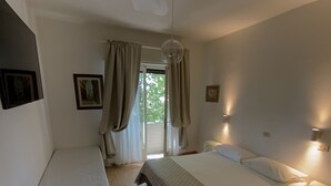 A bedroom with a bed, a desk, and a chair. There is a window with curtains, a ceiling fan, and wall-mounted lights. - Hotel Naviglio (Pietrasanta)
