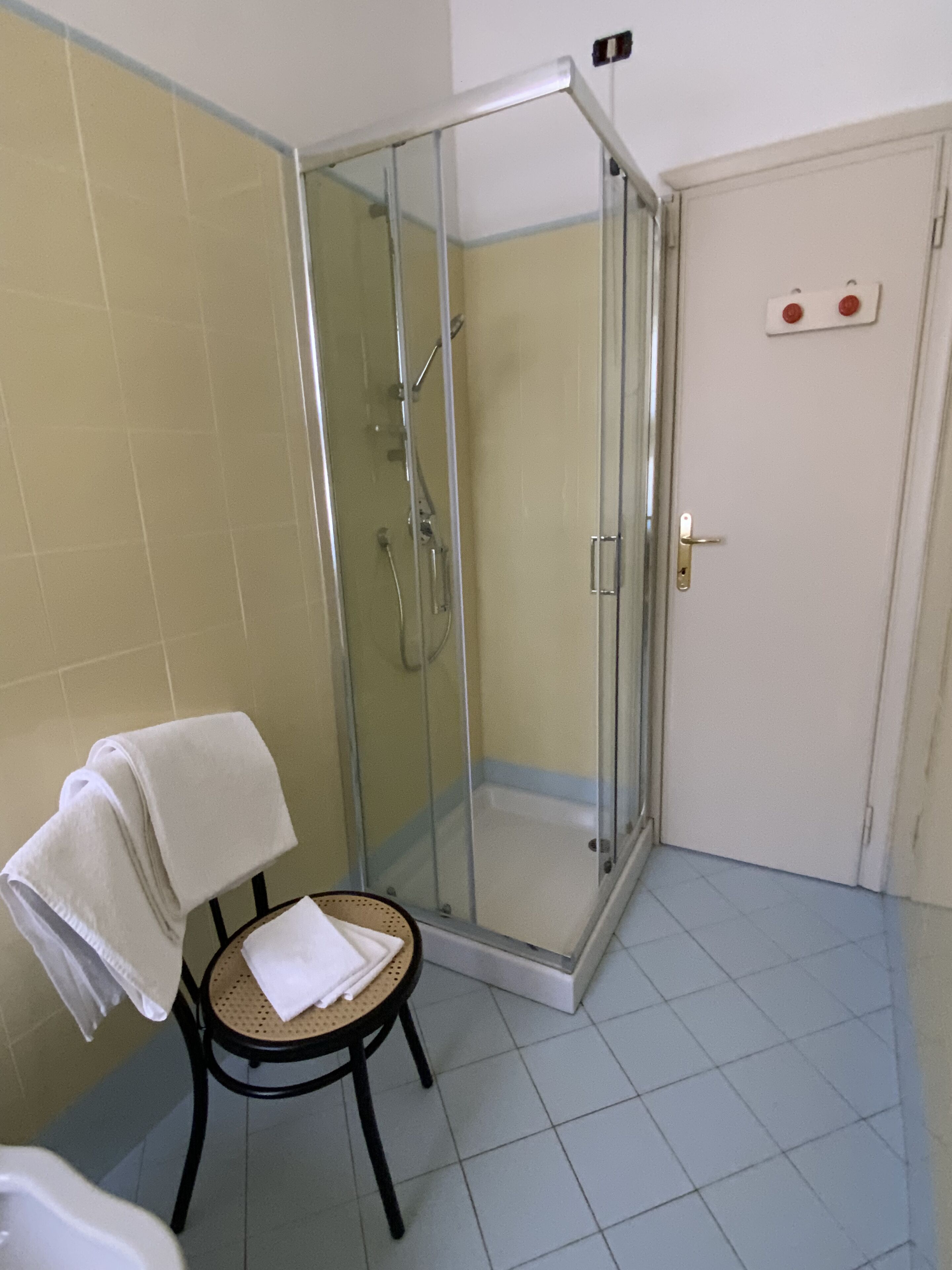 Un baño con cabina de ducha de vidrio, un perchero con una toalla doblada y una pequeña silla de mimbre.