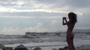 A beach scene with a rocky shoreline and a pier in the background. - Hotel Naviglio (Pietrasanta)