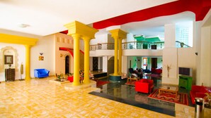 Un vestíbulo amplio con columnas amarillas, asientos rojos y azules, y suelo de mármol.