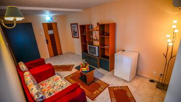 Una sala de estar con un sofá rojo, una mesita con fruta, un televisor y un refrigerador.