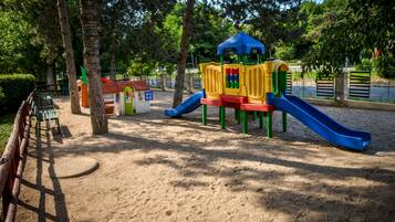 Un parque infantil con tobogán y estructuras para escalar, rodeado de árboles y bancos.