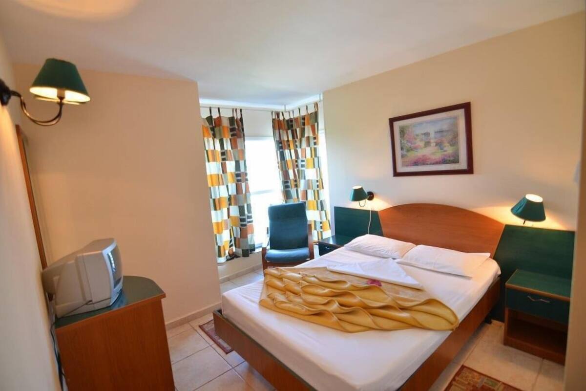 Une chambre d’hôtel avec un lit, une chaise, un bureau avec une lampe et un tableau au mur.