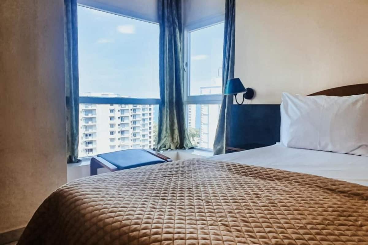 Une chambre d’hôtel avec un lit, un bureau et une vue sur les bâtiments, visible à travers de grandes fenêtres.