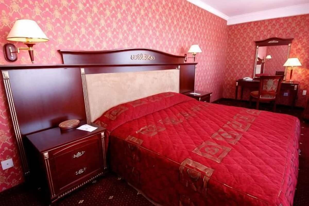 Hotellihuone, jossa on suuri sänky, yöpöytä, lipasto, työpöytä tuolilla ja peili.