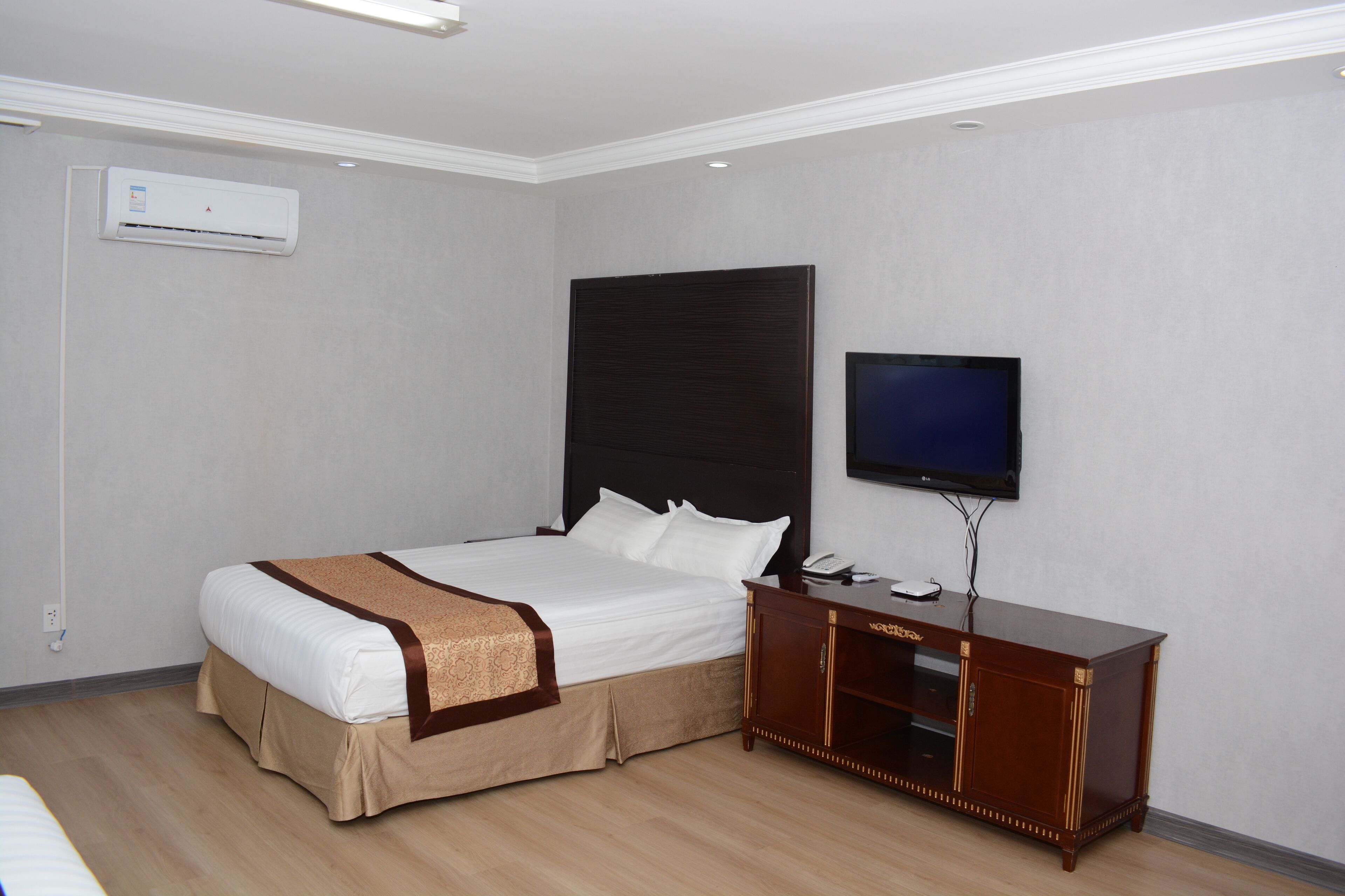 Une chambre d’hôtel avec un lit, une télévision, une commode en bois et un climatiseur fixé au mur.