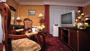 A hotel room with a wooden chair, a desk with a lamp, a television, and a floral arrangement. - White House Hotel (Ulaanbaatar)