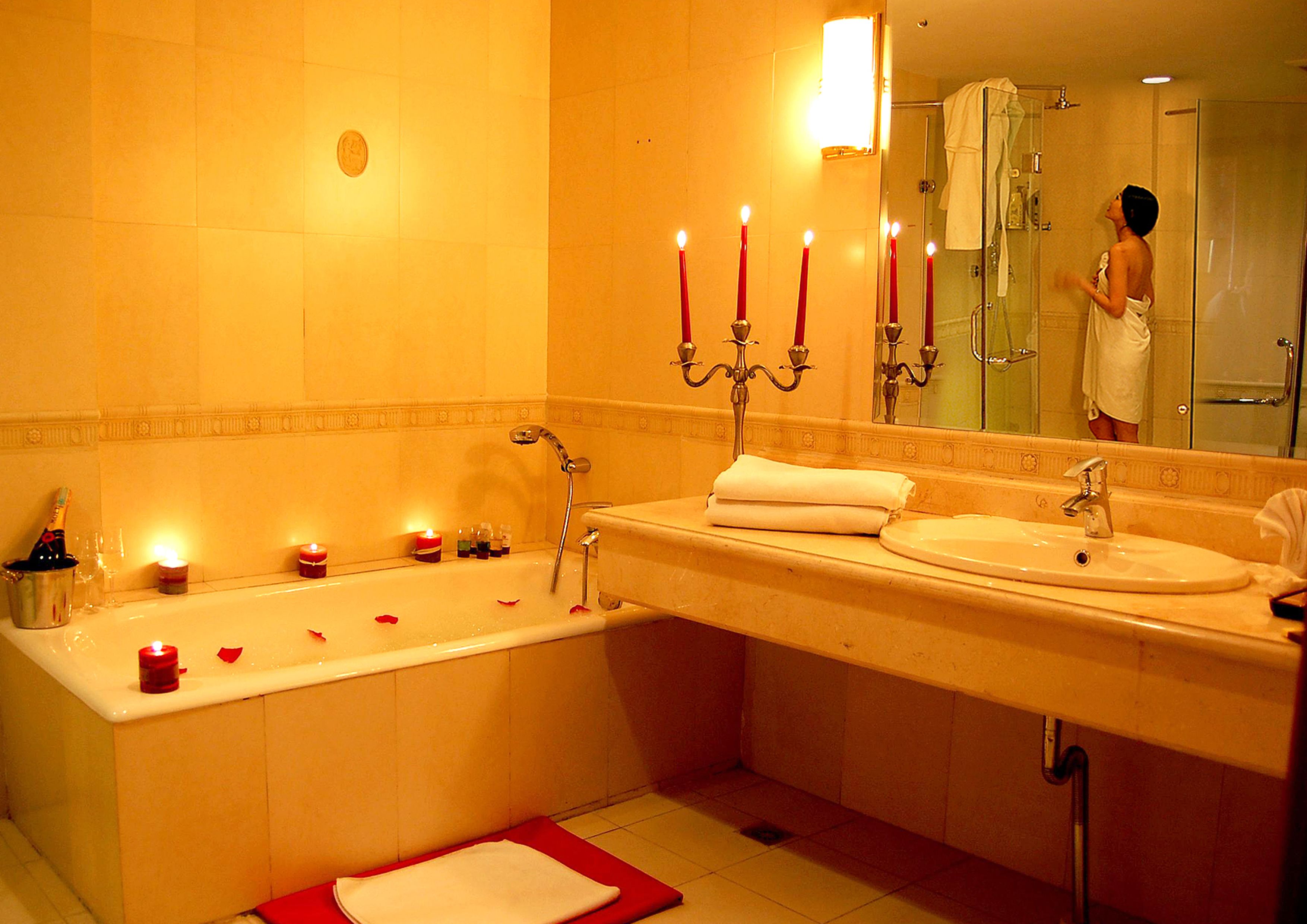Une salle de bain avec une baignoire, un lavabo et un miroir. Il y a des bougies sur le sol et une serviette sur le lavabo.