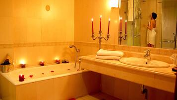 Une salle de bain avec une baignoire, un lavabo et un miroir. Il y a des bougies sur le sol et une serviette sur le lavabo.