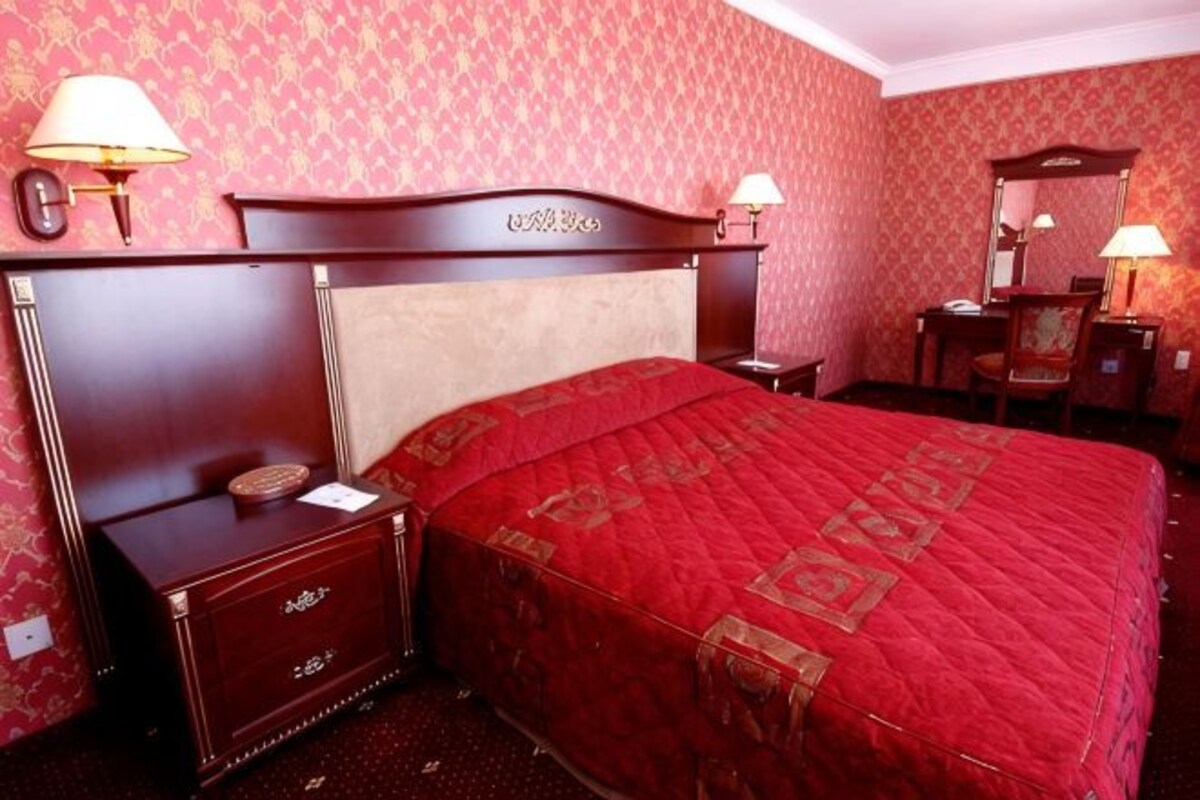 A hotel room with a large bed, a nightstand, a dresser, a desk with a chair, and a mirror.